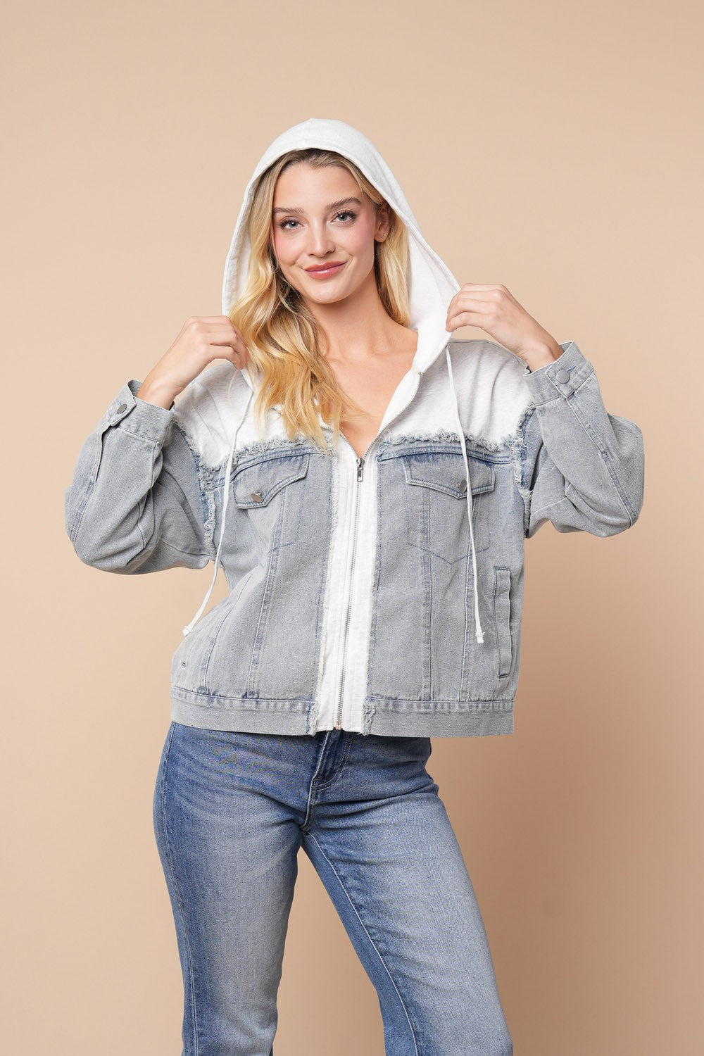 Woman wearing a gray denim jacket with a white hoodie on a beige background