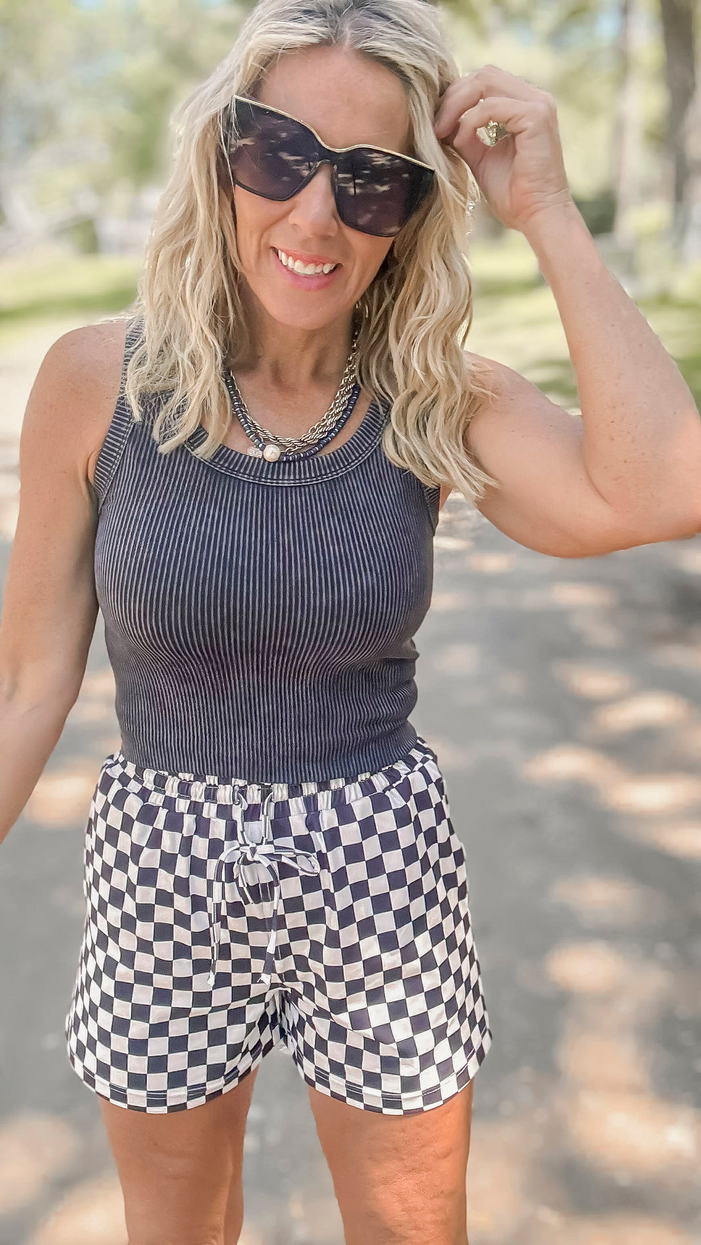 Woman wearing a blue ribbed tank top and checkered shorts outdoors.