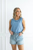 Woman wearing a light blue sleeveless top and denim shorts against a white background