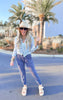 A female model wearing midnight navy everyday joggers with a drawstring waist, a light blue button-up shirt, and white sandals, standing on a road with palm trees in the background.