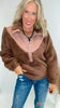 Woman wearing a brown fleece pullover and blue jeans against a white background