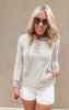 Woman wearing a taupe and white striped henley hoodie with drawstrings, paired with white distressed denim shorts