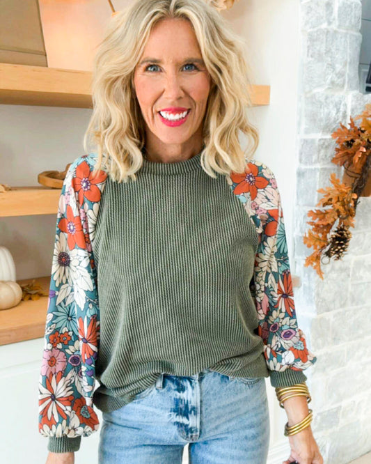 Woman wearing a green ribbed sweater with floral sleeves in a home setting.