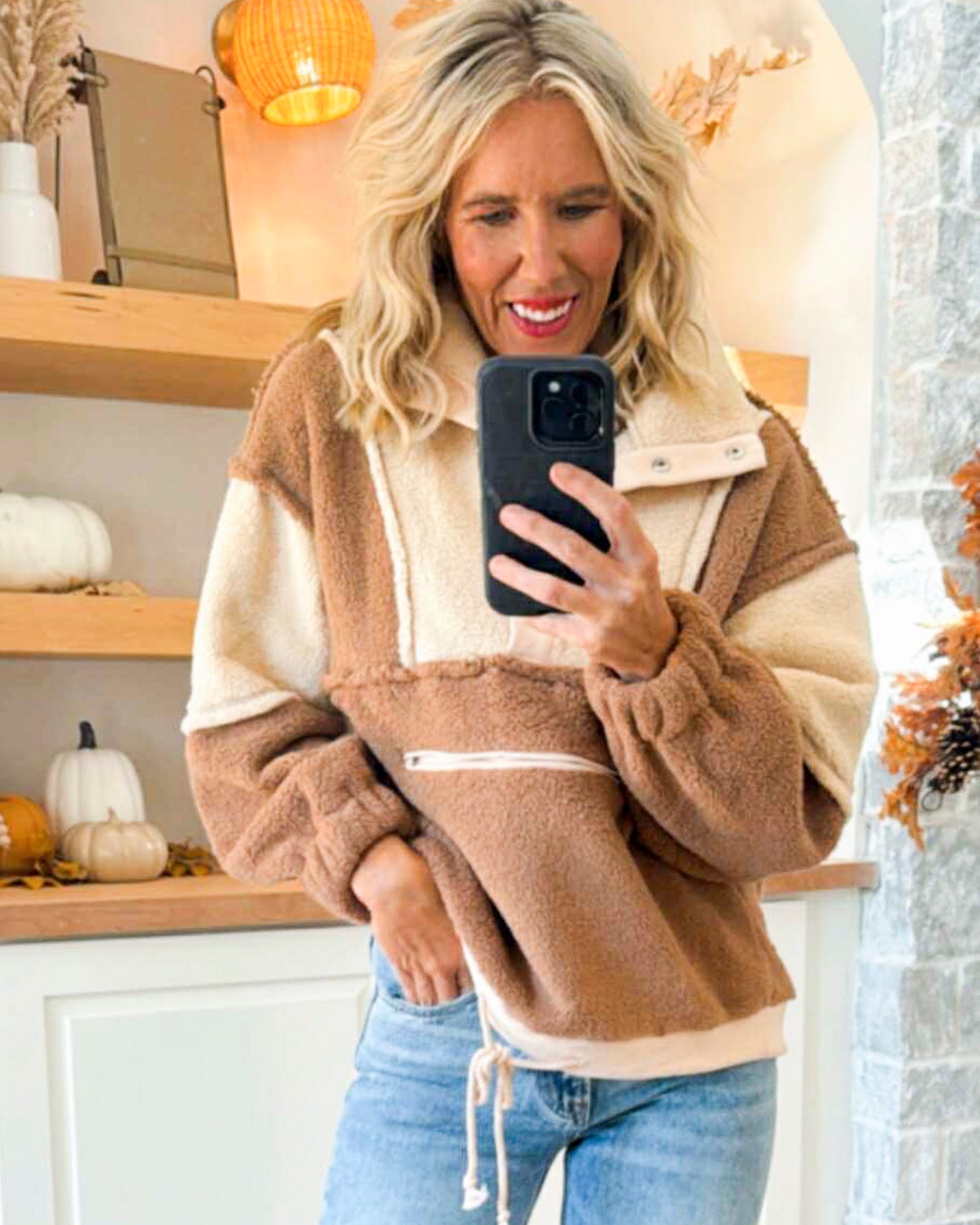 Woman taking a selfie in a cozy indoor setting with pumpkins and decorative lights.