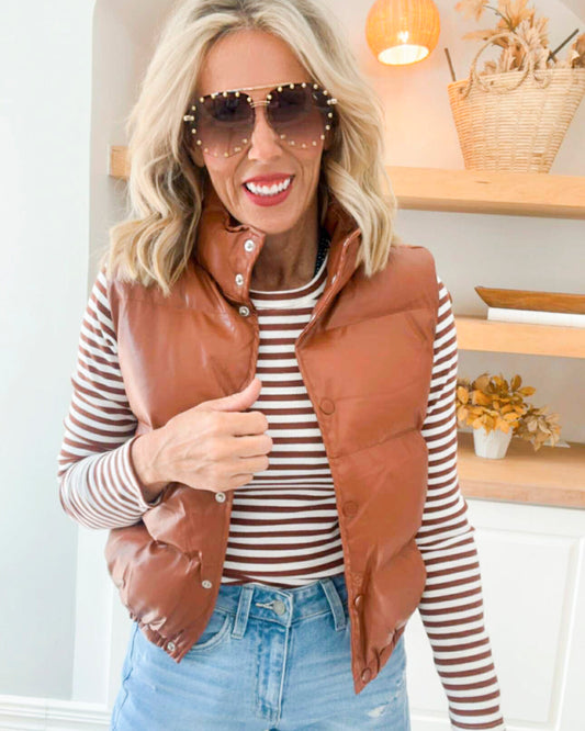 Woman wearing a brown puffer vest over a striped shirt with sunglasses indoors.
