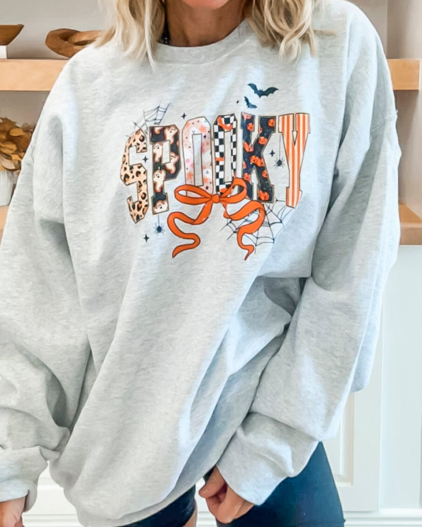 Gray sweatshirt with Halloween-themed design worn by a person indoors.