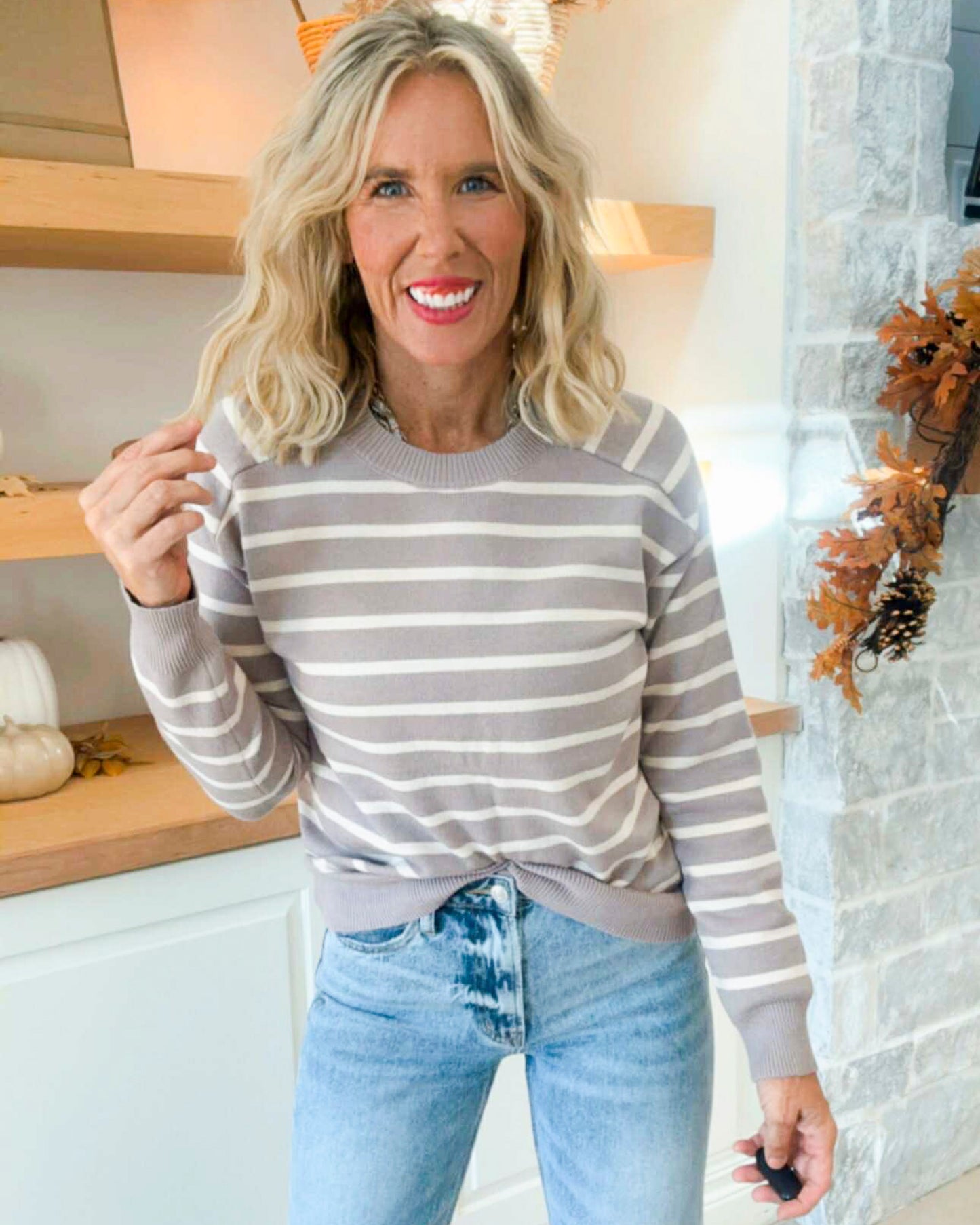 Woman wearing a taupe and white striped sweater and light blue jeans indoors.