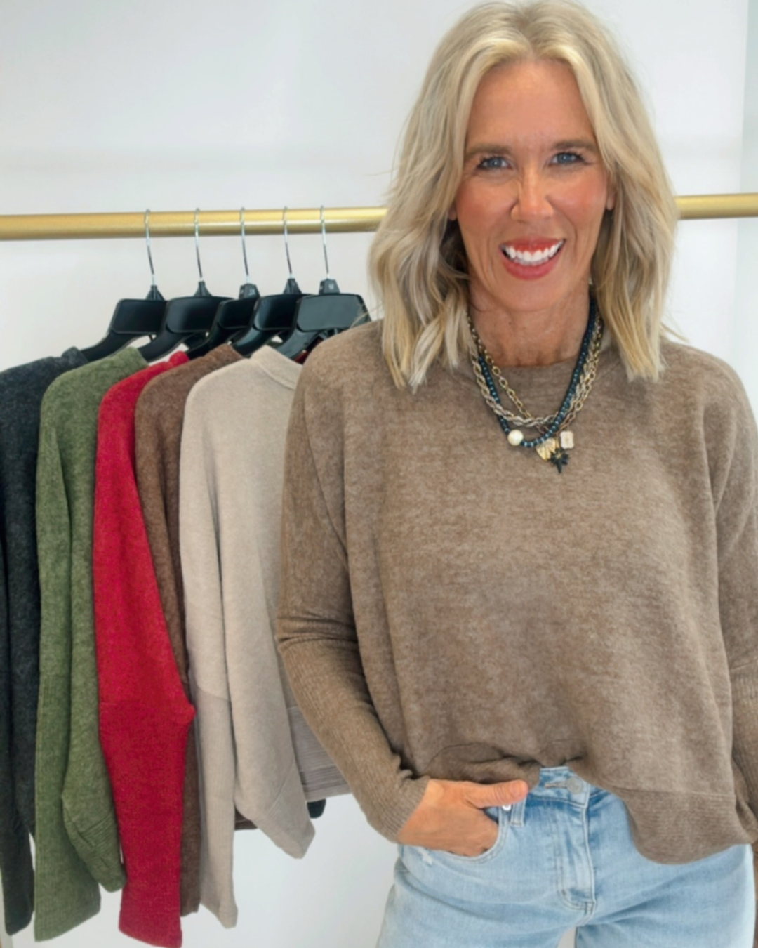 Woman wearing a brown sweater with a rack of sweaters in the background