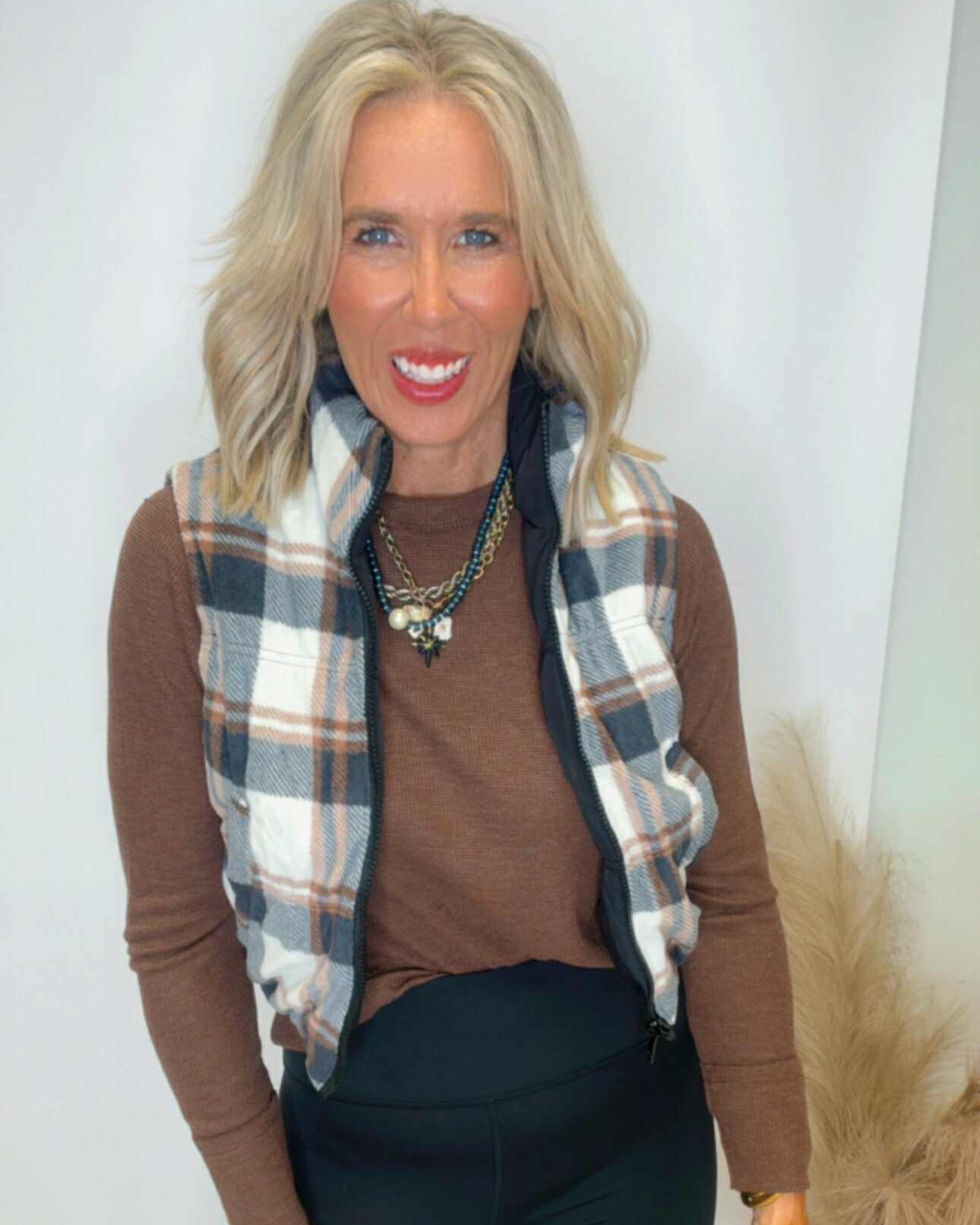 Woman wearing a plaid scarf, brown sweater, and dark pants against a white background