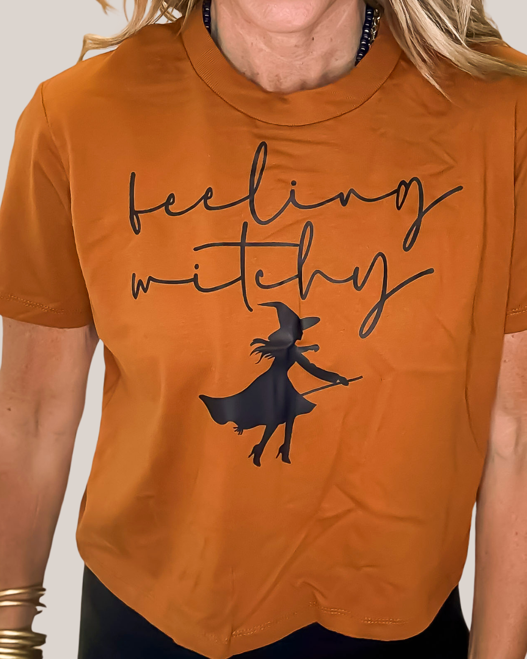 Orange t-shirt with a witch graphic and 'feeling witchy' text on a plain background