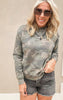 Woman wearing a camo print crewneck sweatshirt with front pocket and dark wash frayed denim shorts.