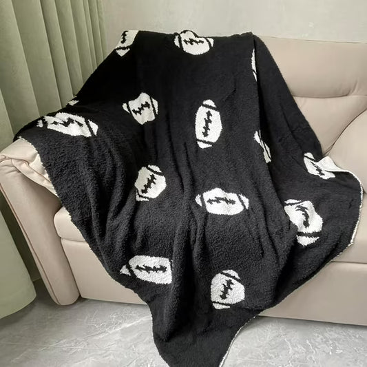 Black blanket with white football patterns draped over a beige sofa.