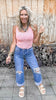 Woman wearing a pink tank top and blue jeans standing in front of a wooden wall.