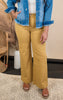 A model wearing a high-rise wide trouser in yellow, paired with a denim jacket and standing in a room with natural lighting.