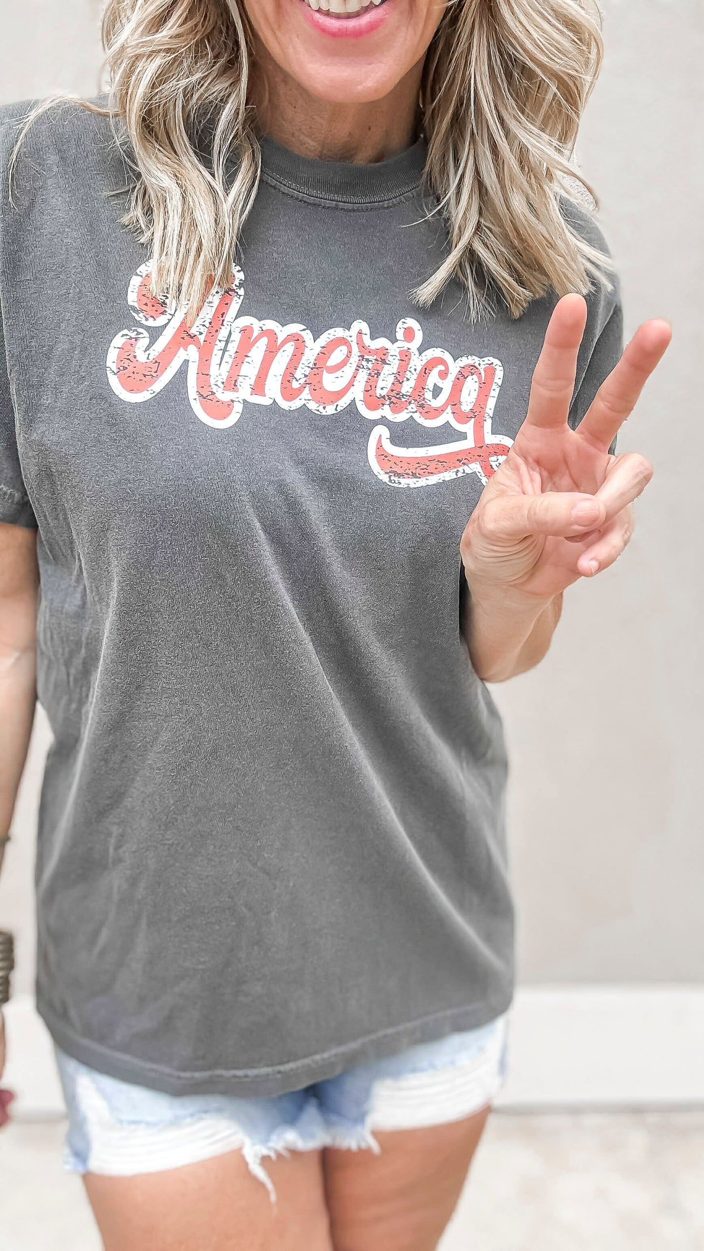 Vintage-style America graphic tee with faded red script and distressed denim shorts.