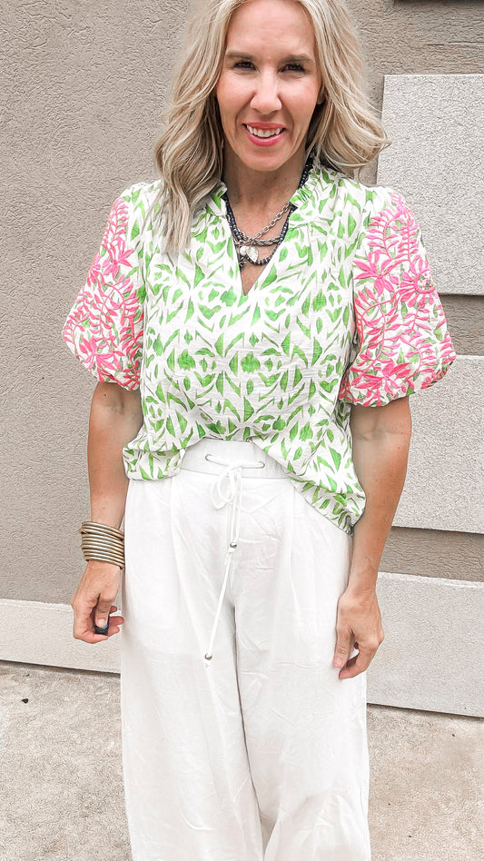 Pink and green floral embroidered bubble sleeve top with white pants.