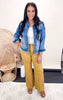 A model wearing a high-rise wide trouser in yellow, paired with a denim jacket and standing in a room with natural lighting.