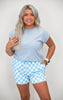Woman wearing a light blue t-shirt and checkered shorts on a plain background