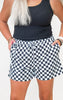 Person wearing black tank top and checkered shorts on a plain background