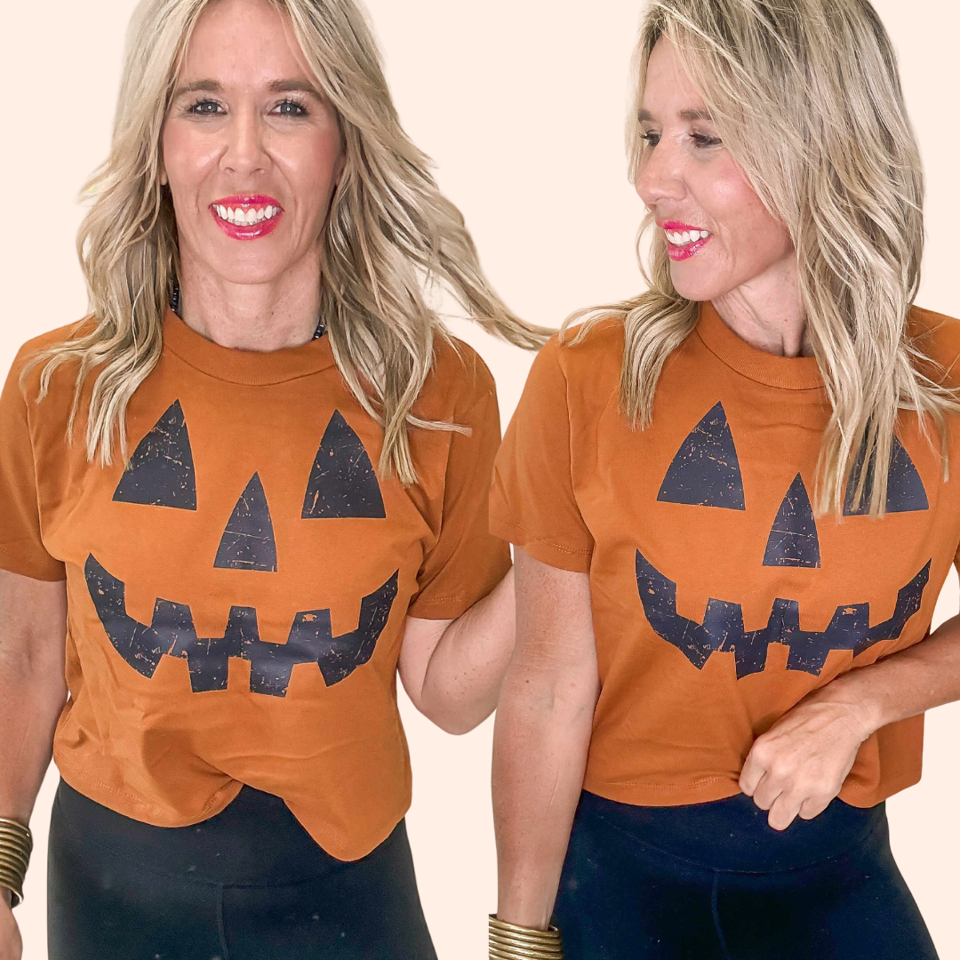 Woman wearing an orange t-shirt with a jack-o'-lantern face design on a beige background