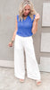 Stylish outfit featuring a vibrant knit tank and comfy white drawstring pants, with soft beachy waves and neutral sandals.