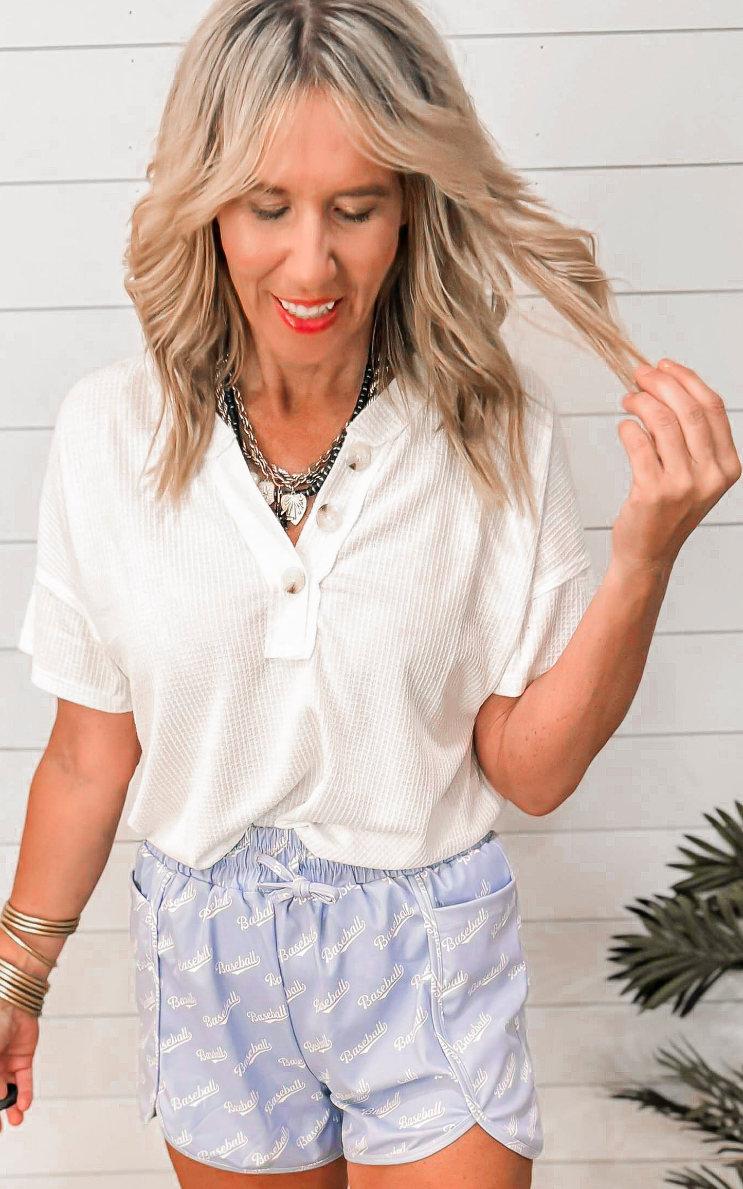Woman wearing a white blouse and light blue shorts with a white wooden background