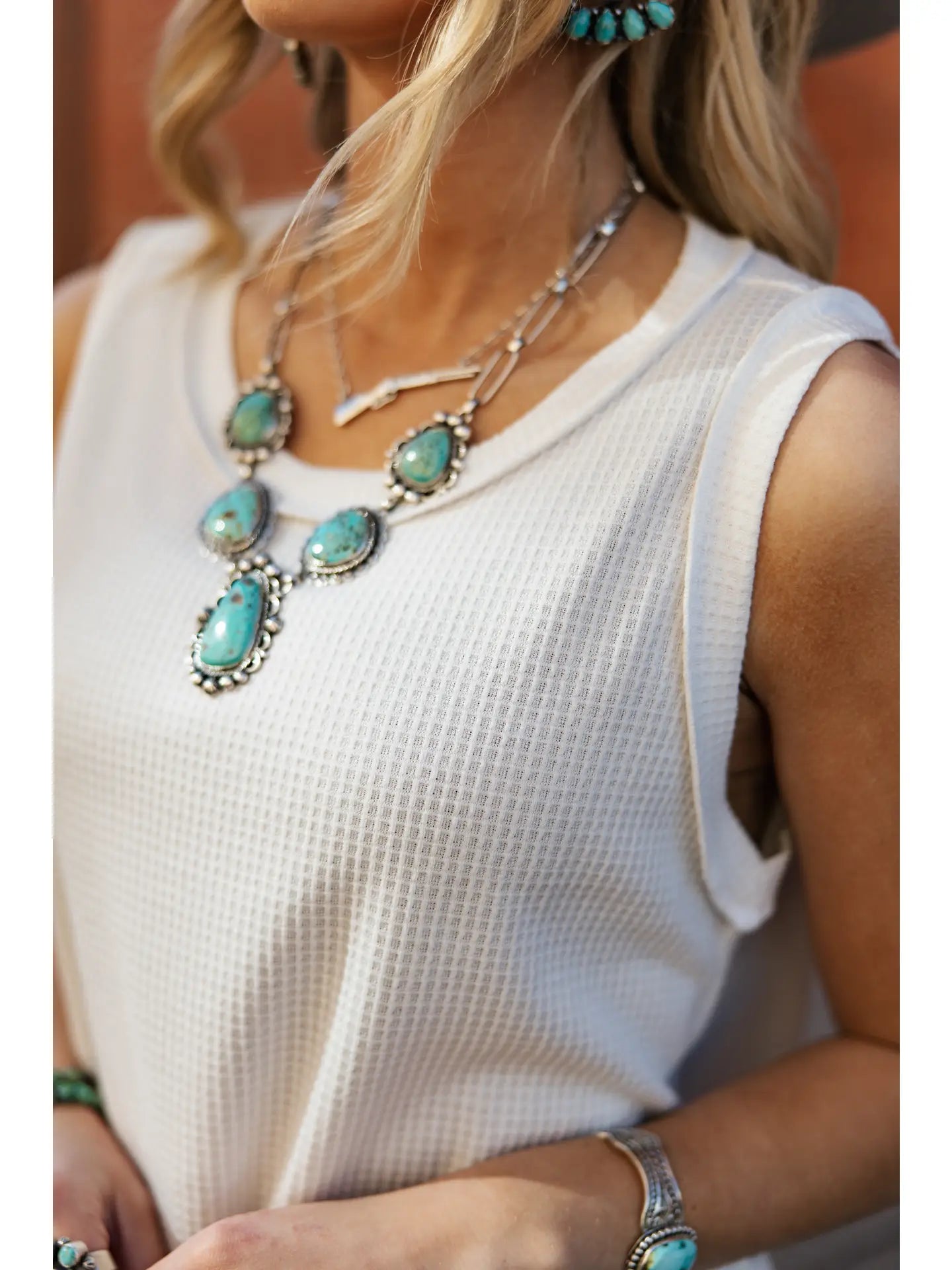 Woman wearing a white sleeveless top with turquoise jewelry