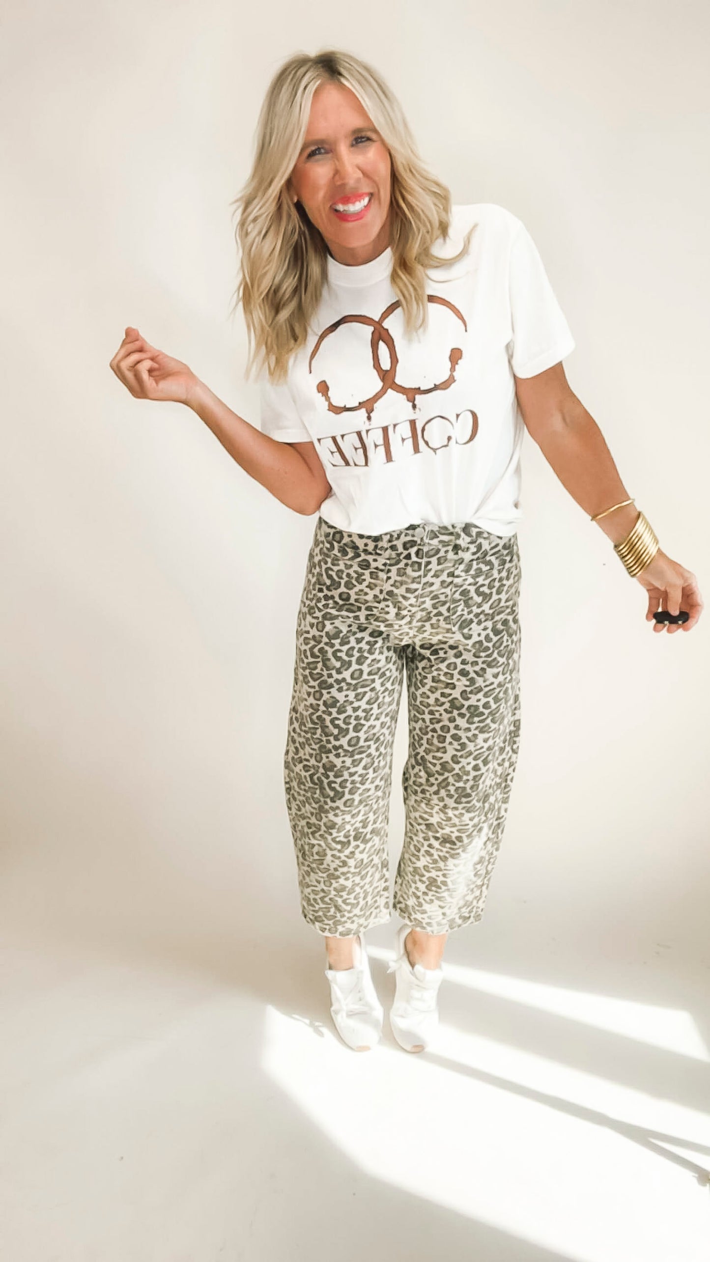 Woman wearing a white t-shirt with text and leopard print pants on a plain background