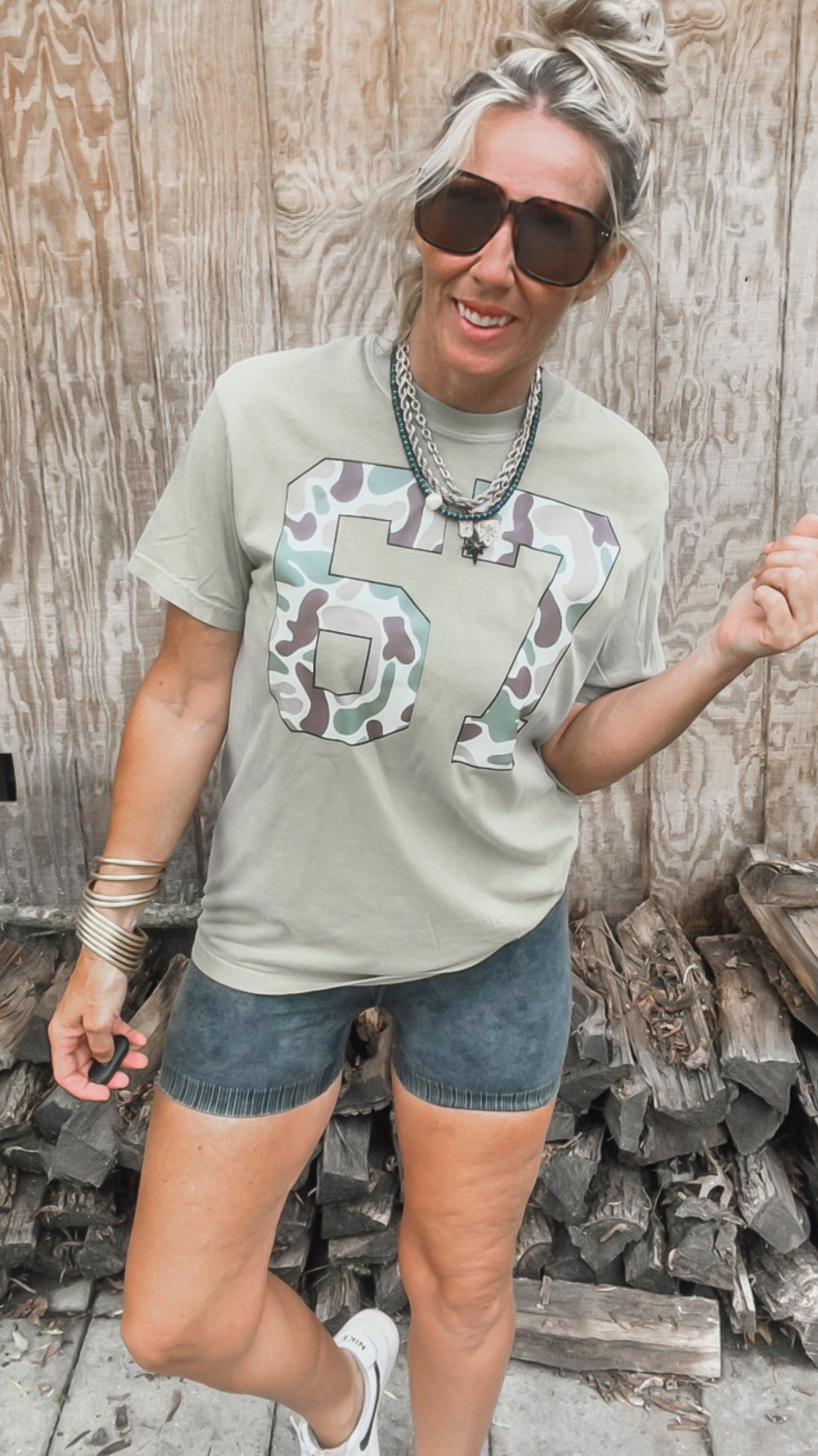 Person wearing a t-shirt with a camouflage number design, standing in front of wooden planks.