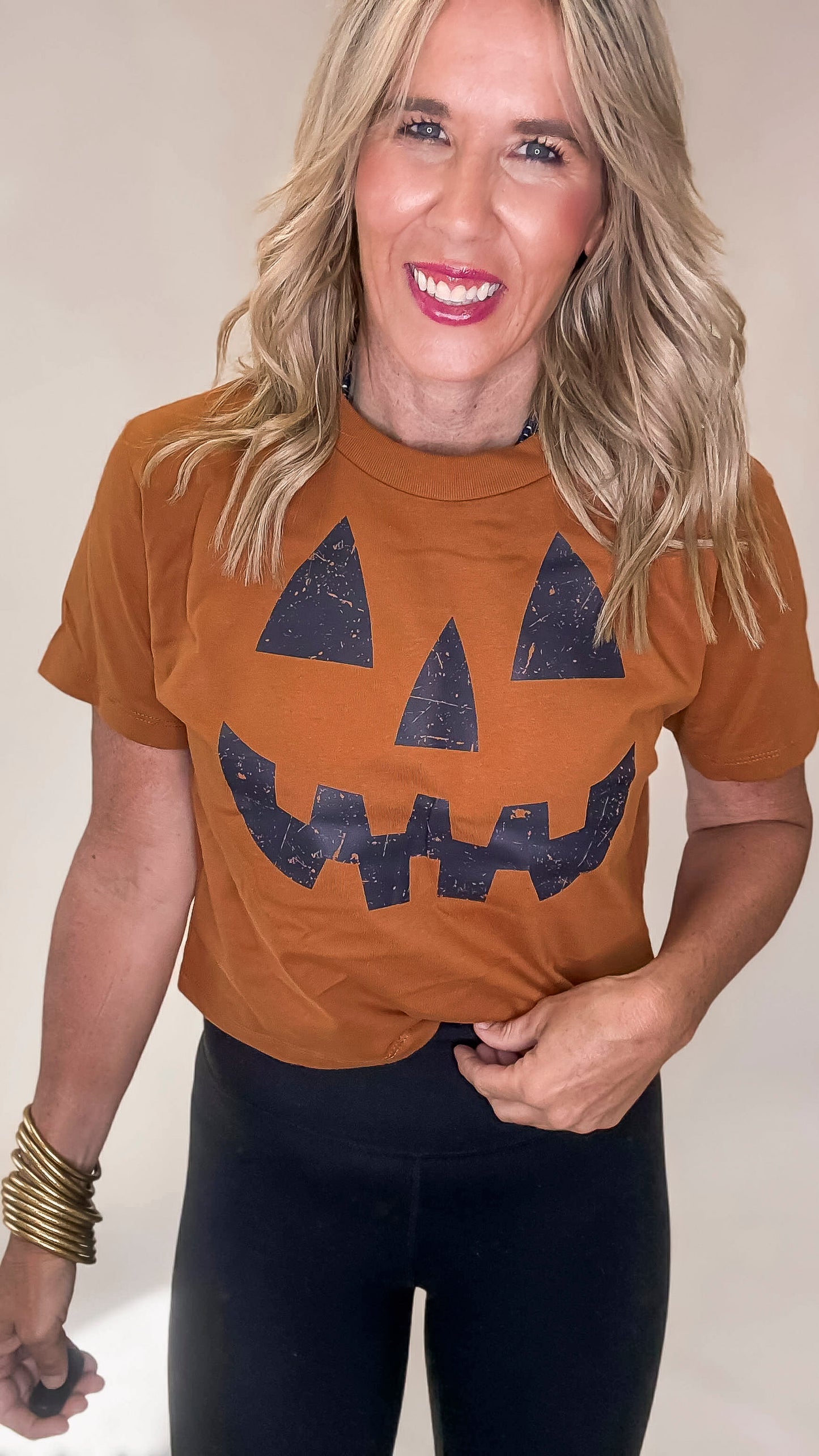 Woman wearing a brown t-shirt with a jack-o'-lantern design on a plain background