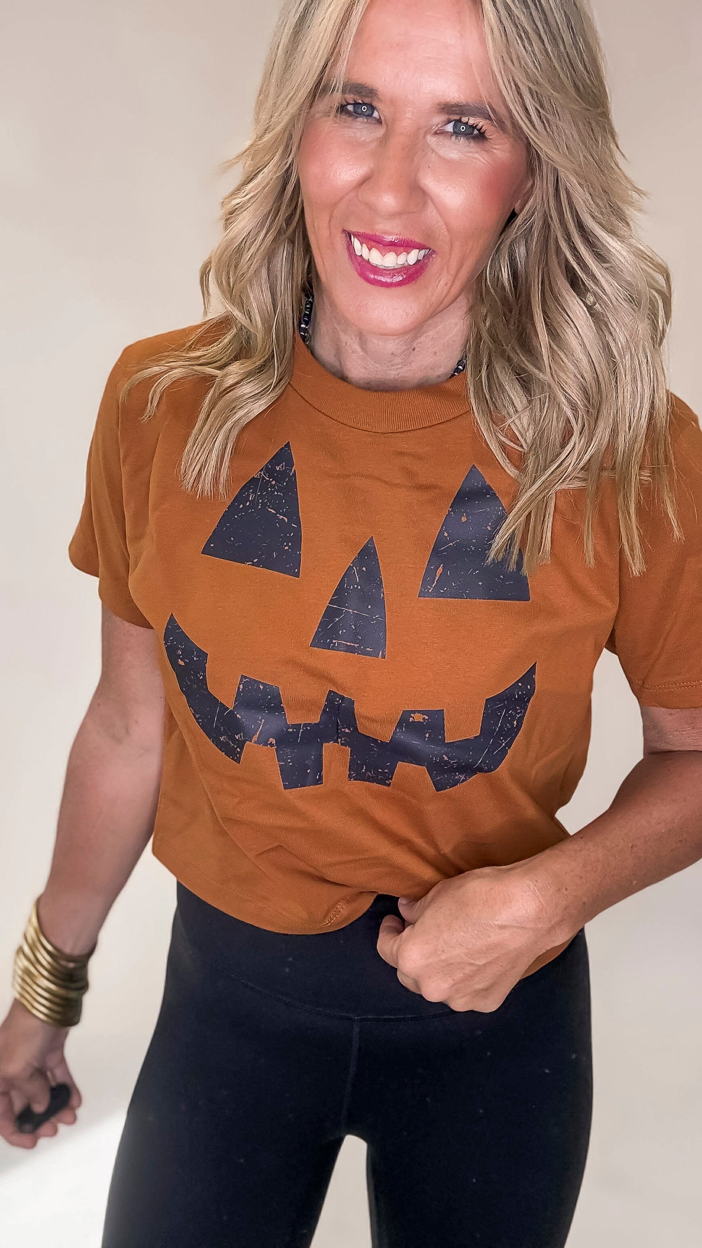 Woman wearing a brown t-shirt with a jack-o'-lantern face design on a plain background