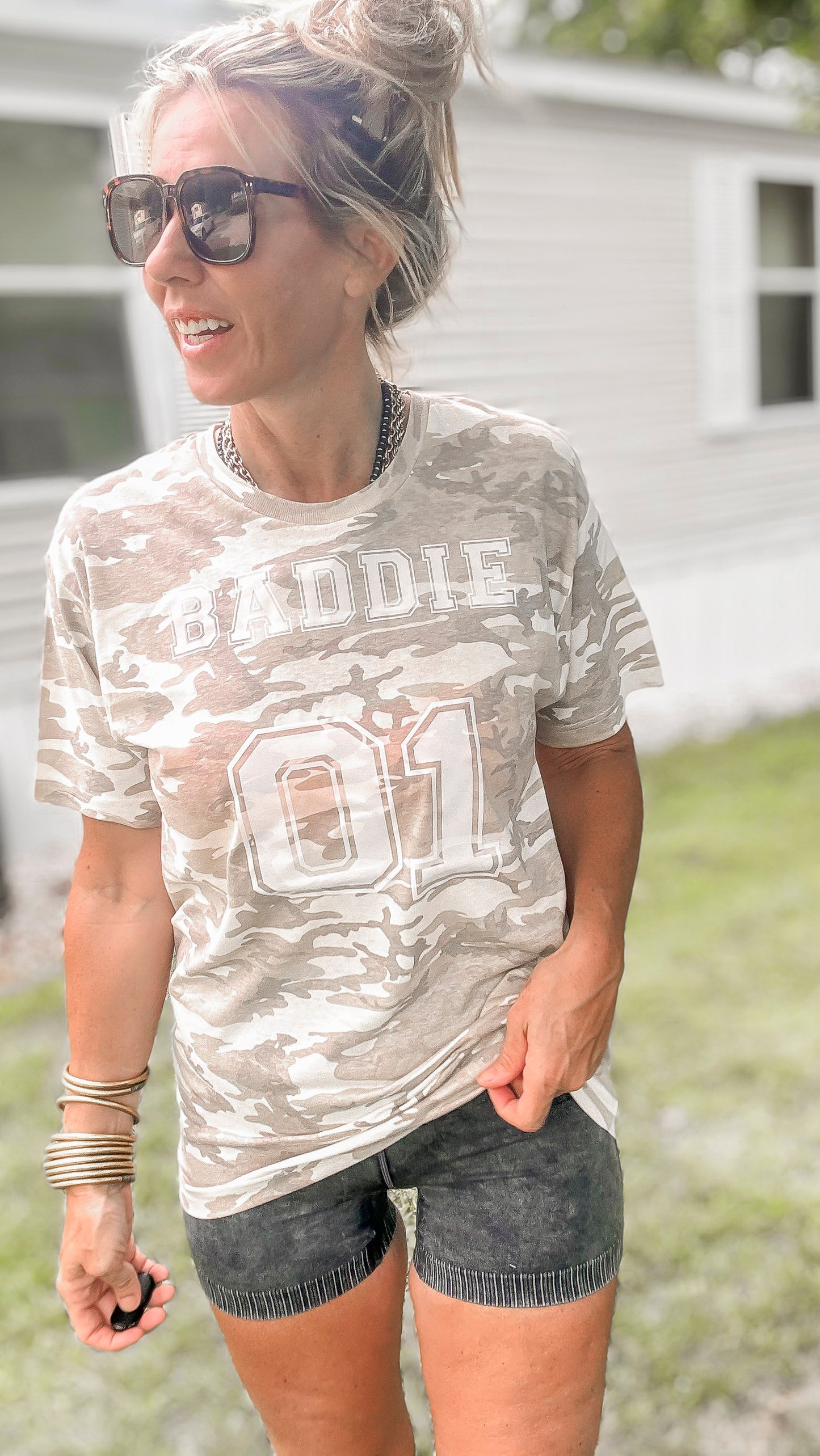 Woman wearing a camouflage t-shirt with text outdoors