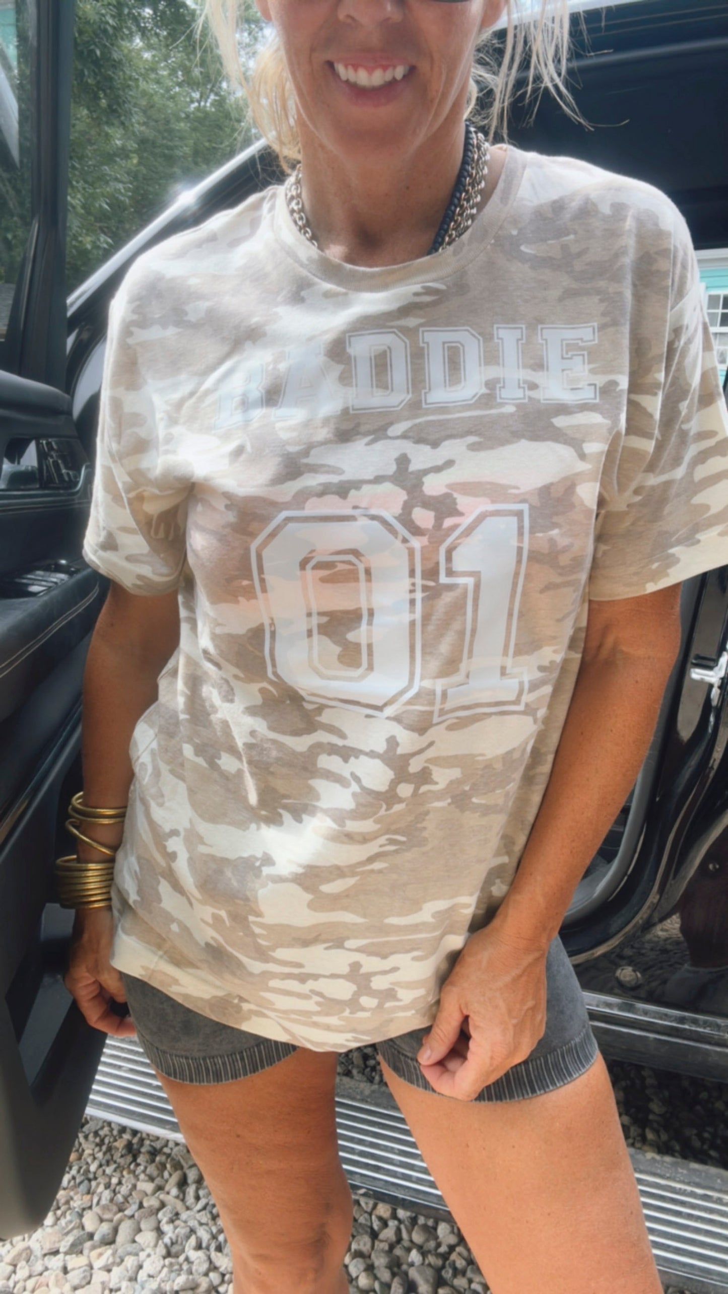 Person wearing a camouflage-patterned t-shirt with 'ODIE' and number '01' text, standing next to a vehicle.