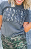 Person wearing a gray t-shirt with text and camouflage pants against a light background