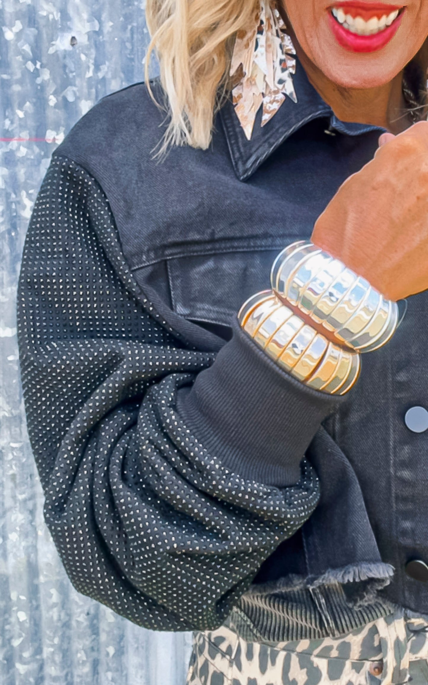 Person wearing a black textured jacket with gold bangles on a blurred background