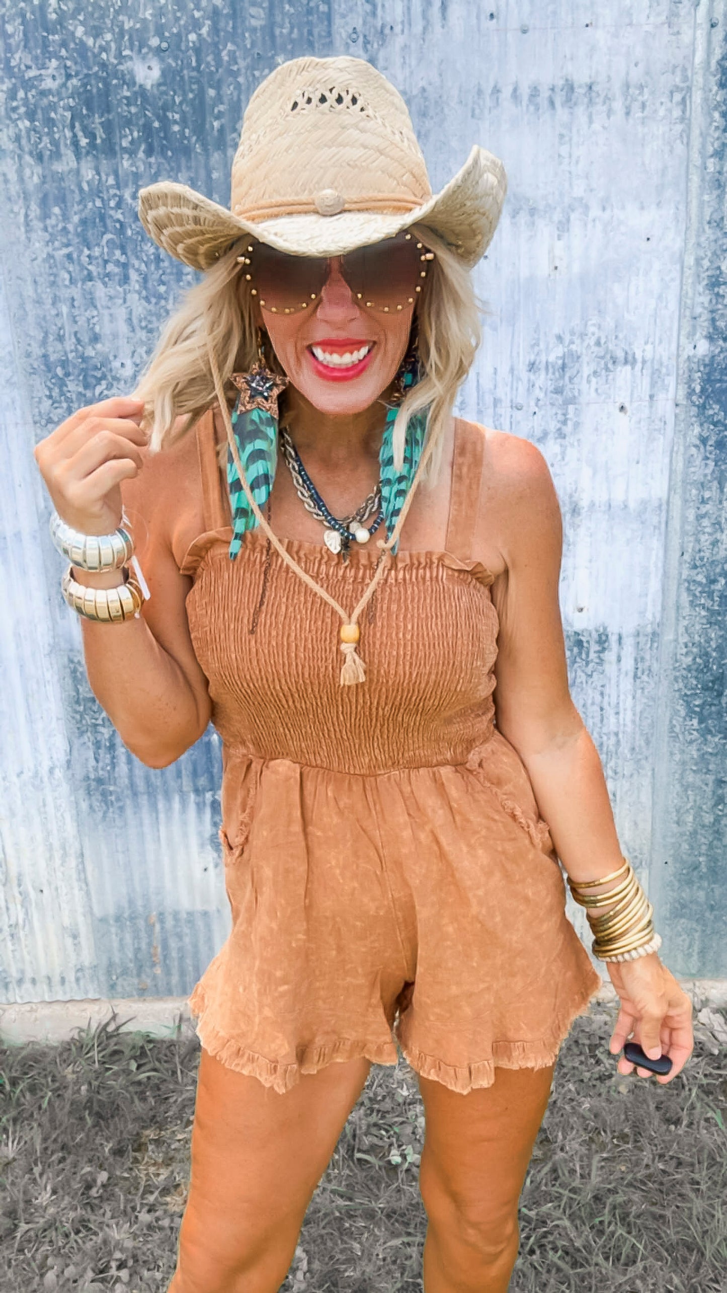 Woman wearing a brown romper and straw hat against a textured wall.