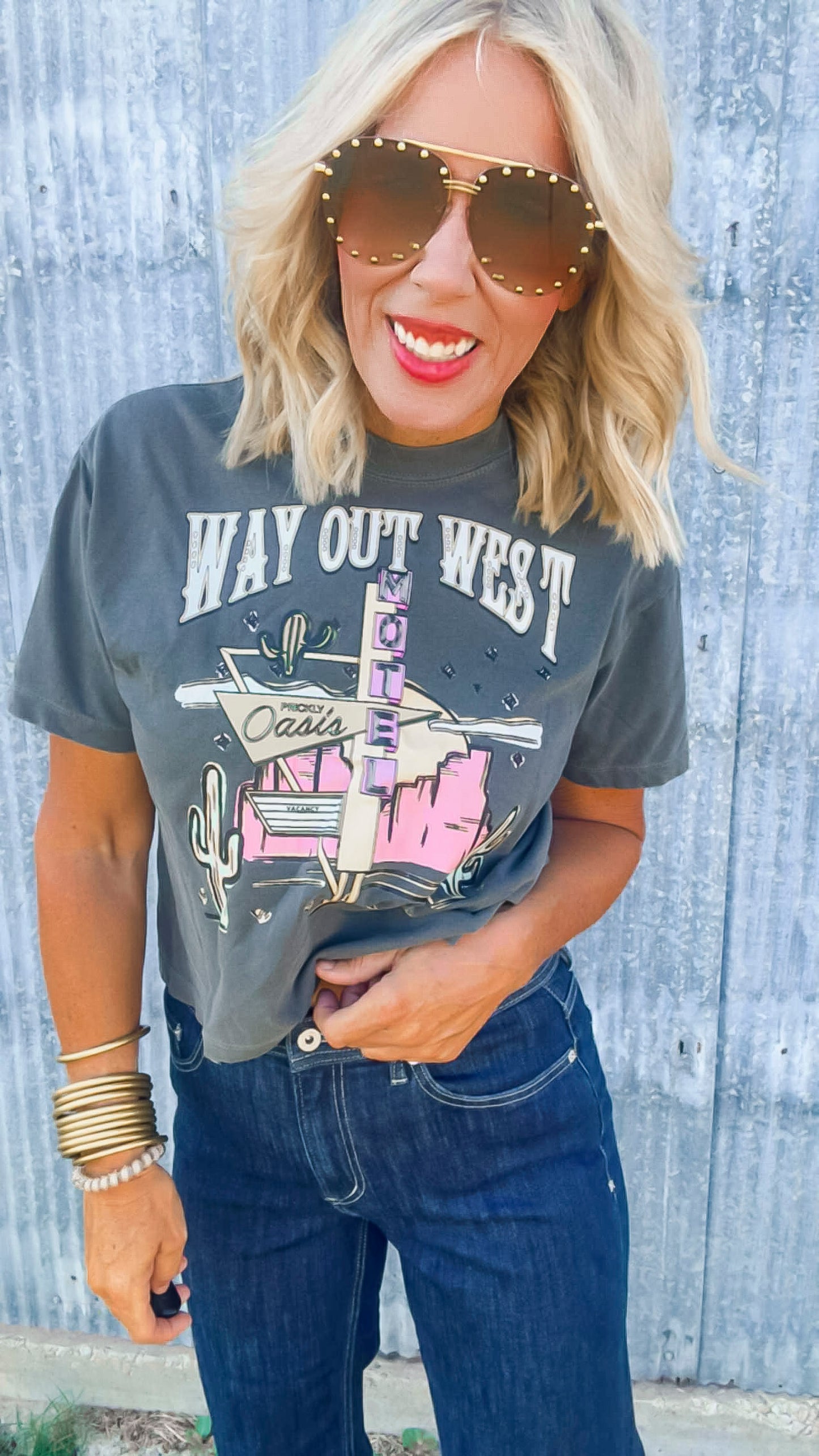 Woman wearing a 'Way Out West' t-shirt with sunglasses and a wooden background