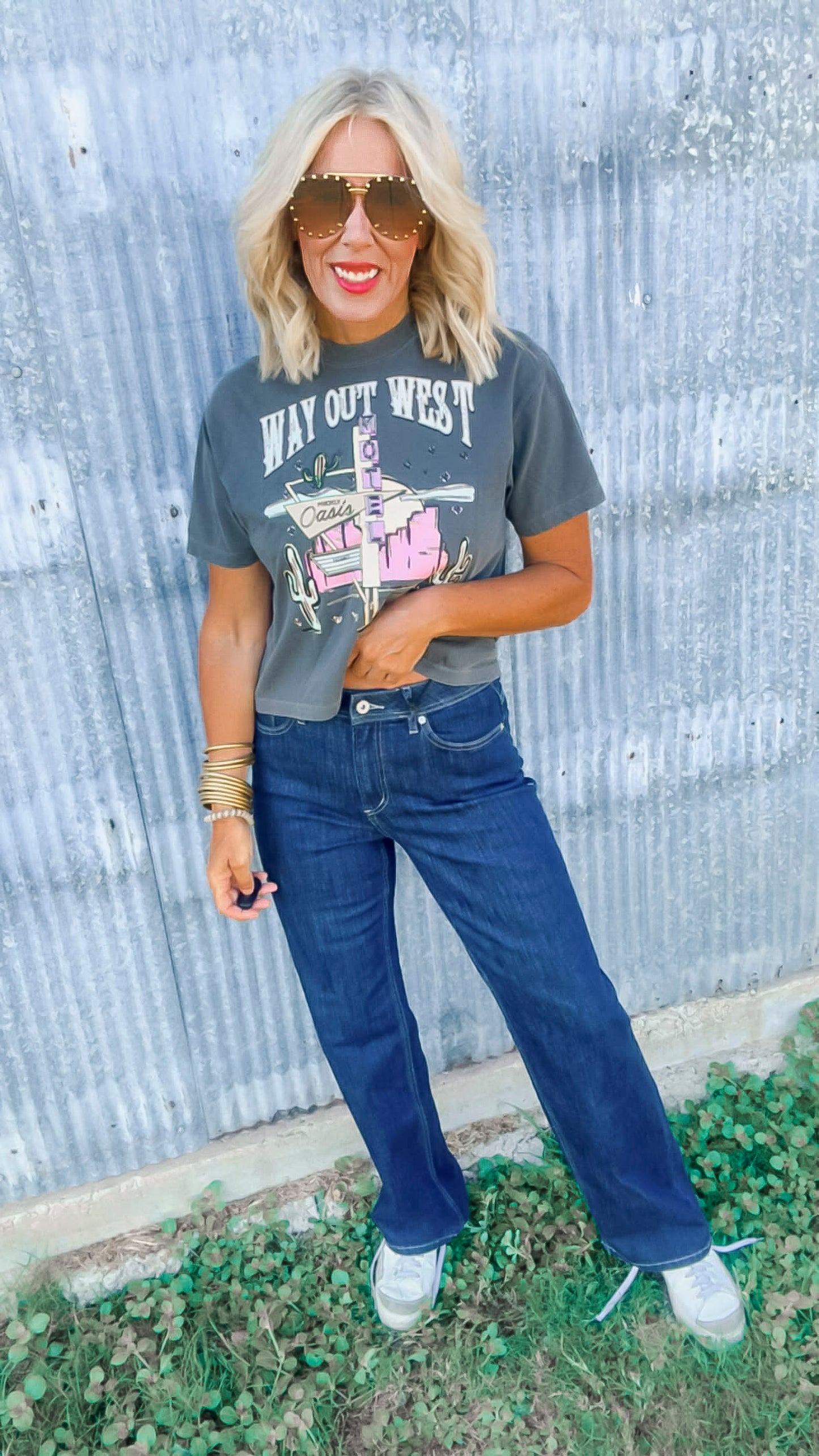 Woman wearing a graphic t-shirt and blue jeans standing in front of a corrugated metal wall.