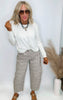 Woman wearing a white top and patterned pants with sunglasses on a plain background