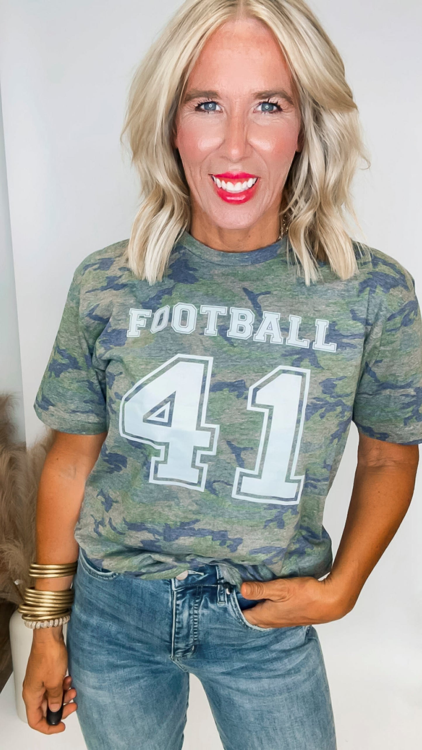 Person wearing a camouflage t-shirt with 'FOOTBALL 41' text on a plain background