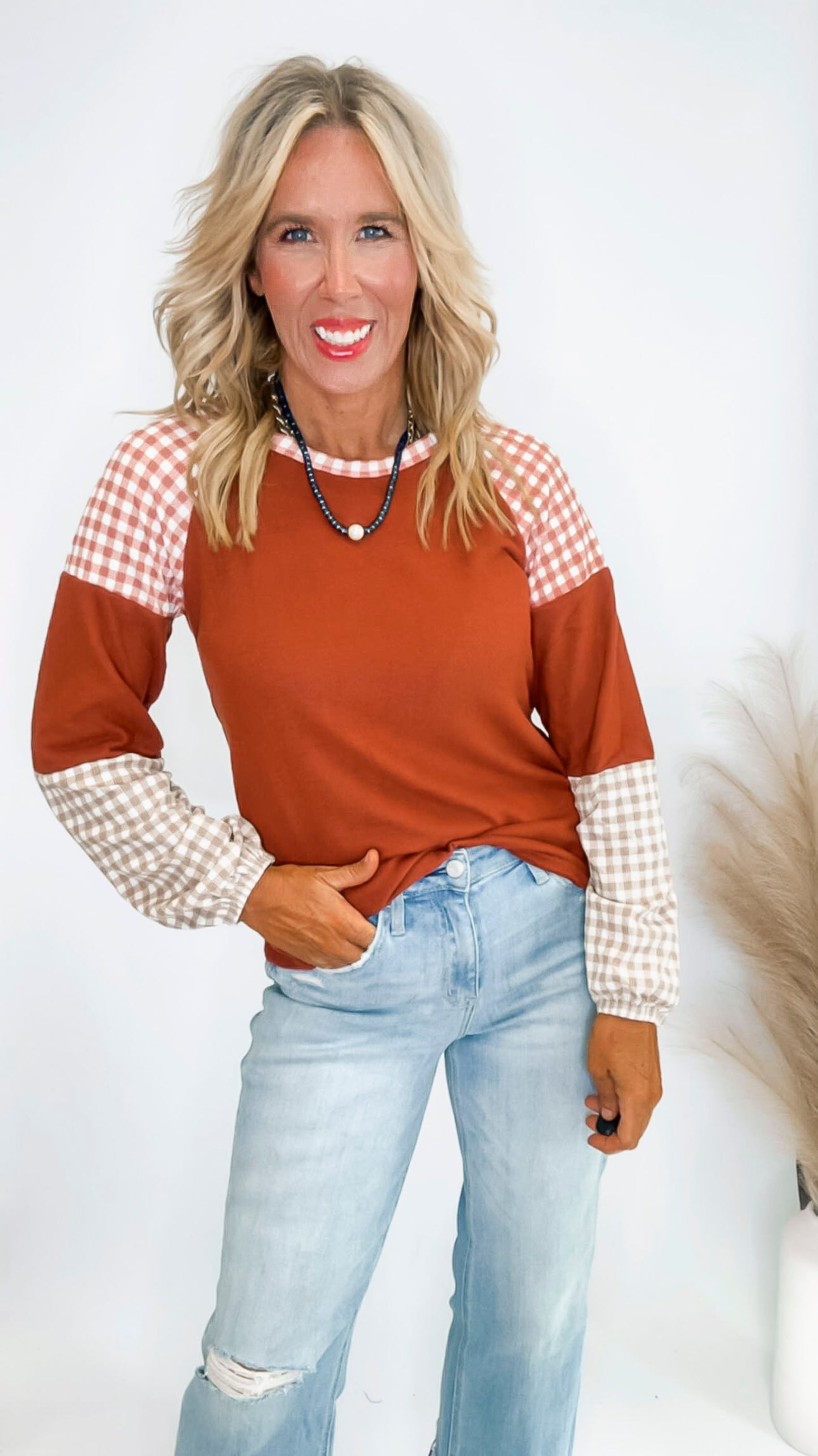 Woman wearing a brown and white checkered top with light blue jeans on a white background