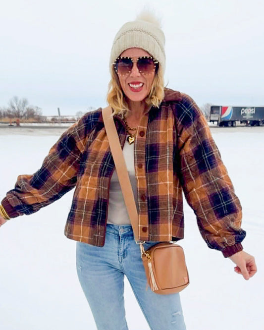 Person wearing a plaid shirt, jeans, and a beanie with sunglasses on a snowy background.