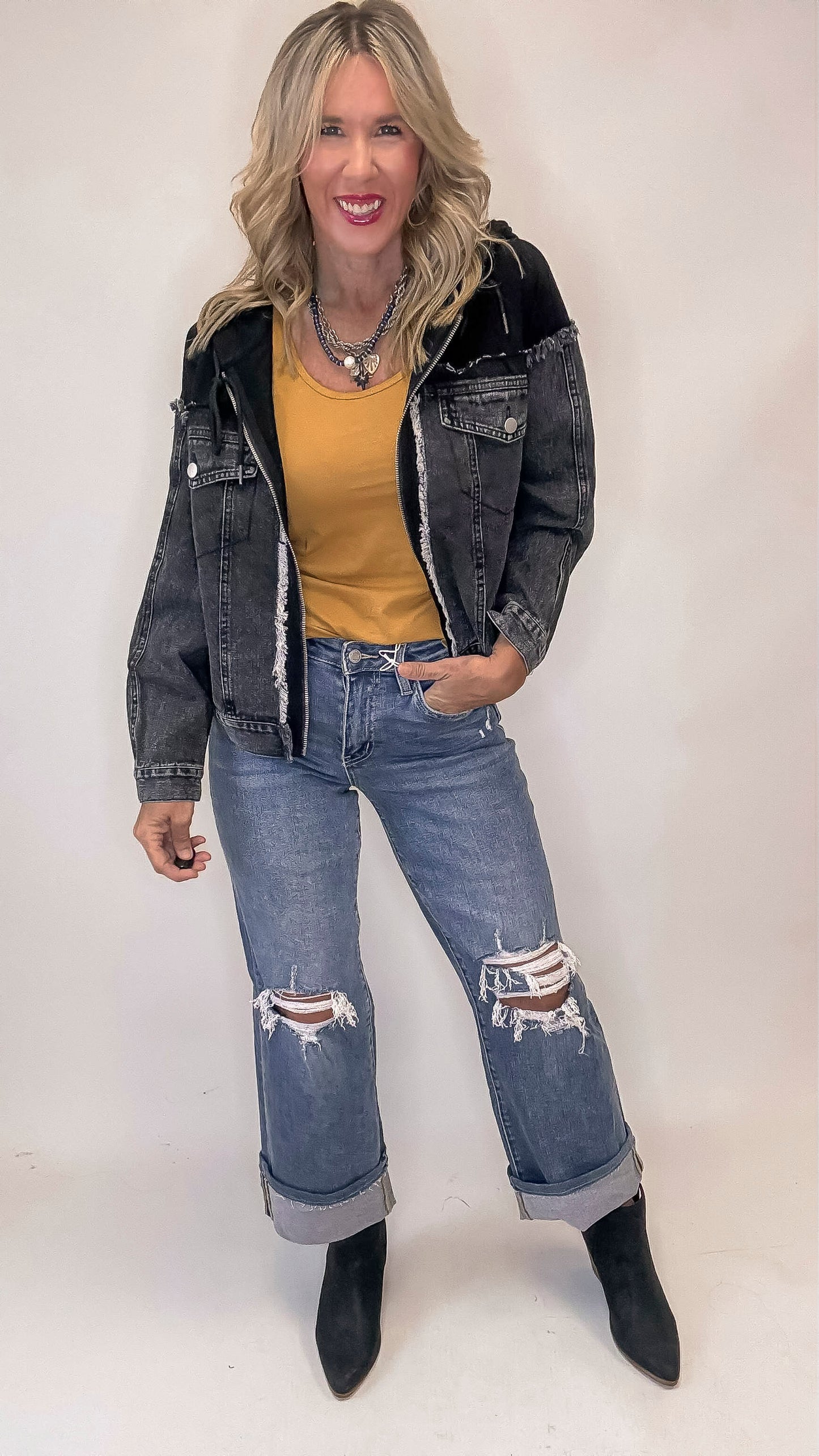Woman wearing a black denim jacket, yellow top, and distressed jeans on a white background