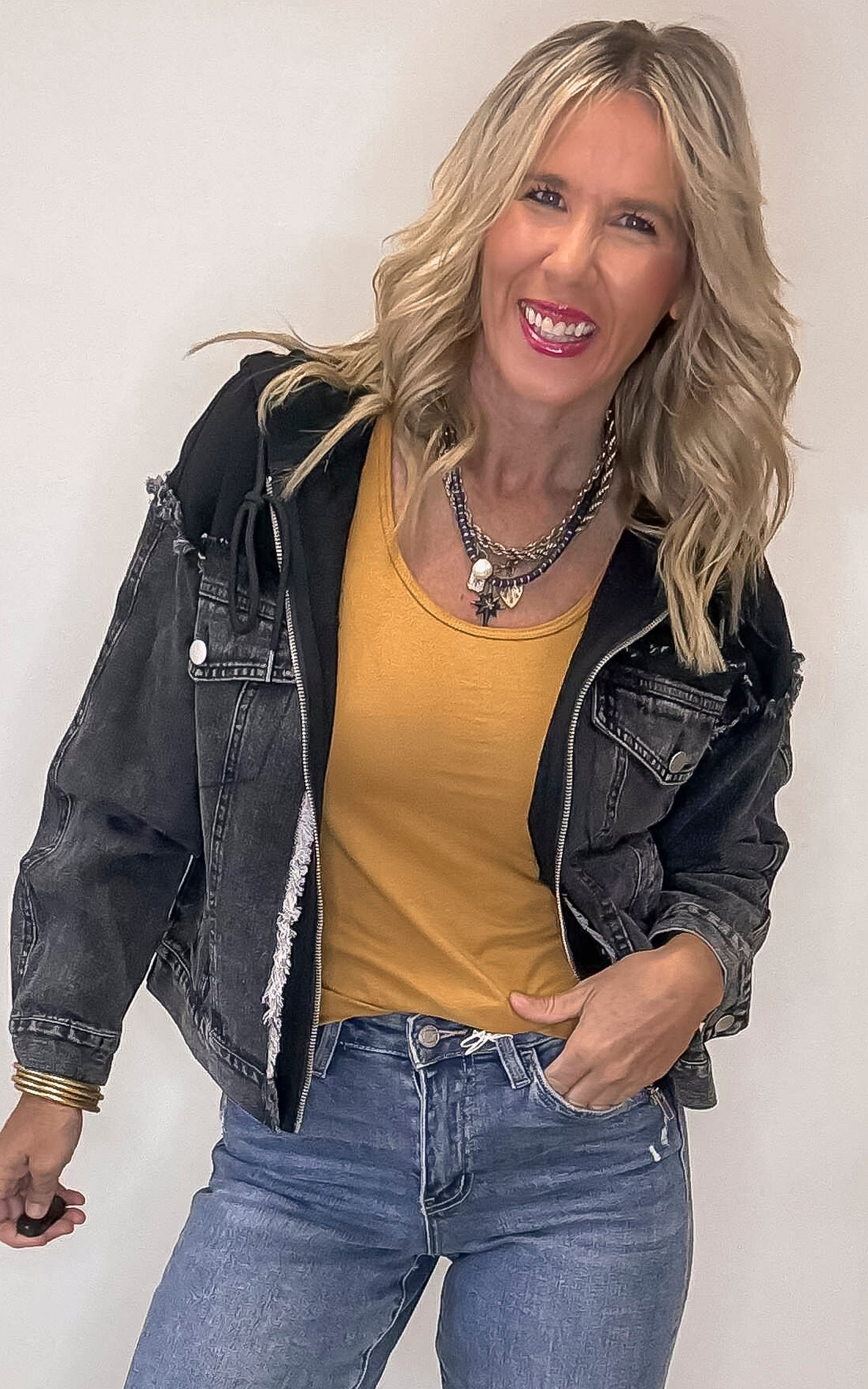 Woman wearing a black denim jacket, yellow top, and blue jeans against a white background