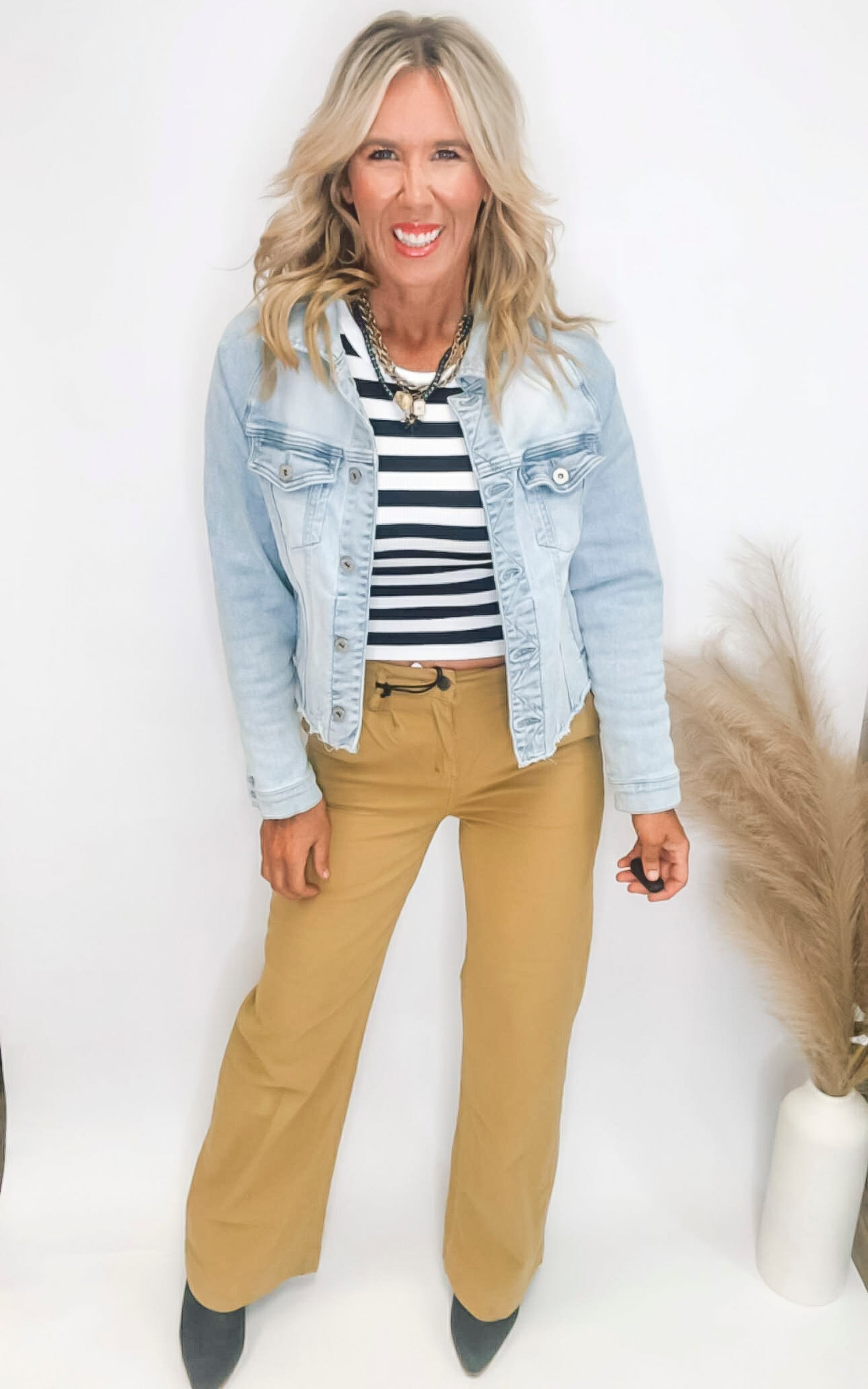 Woman wearing a striped shirt, denim jacket, and beige pants on a white background