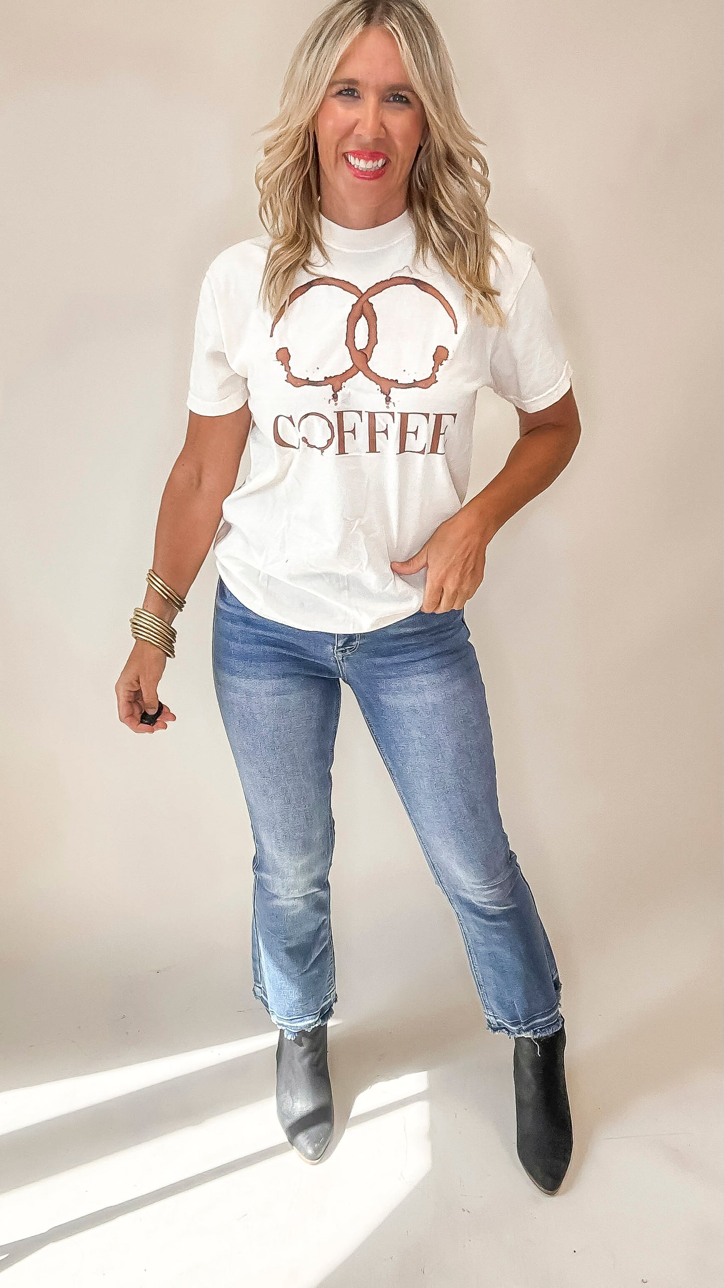 Woman wearing a white t-shirt with 'Coffee' design and blue jeans on a plain background