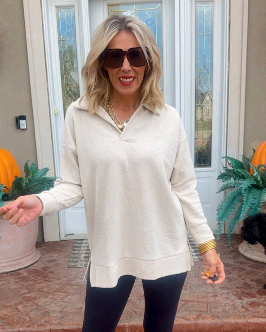 Woman wearing a beige long-sleeve top and sunglasses indoors.