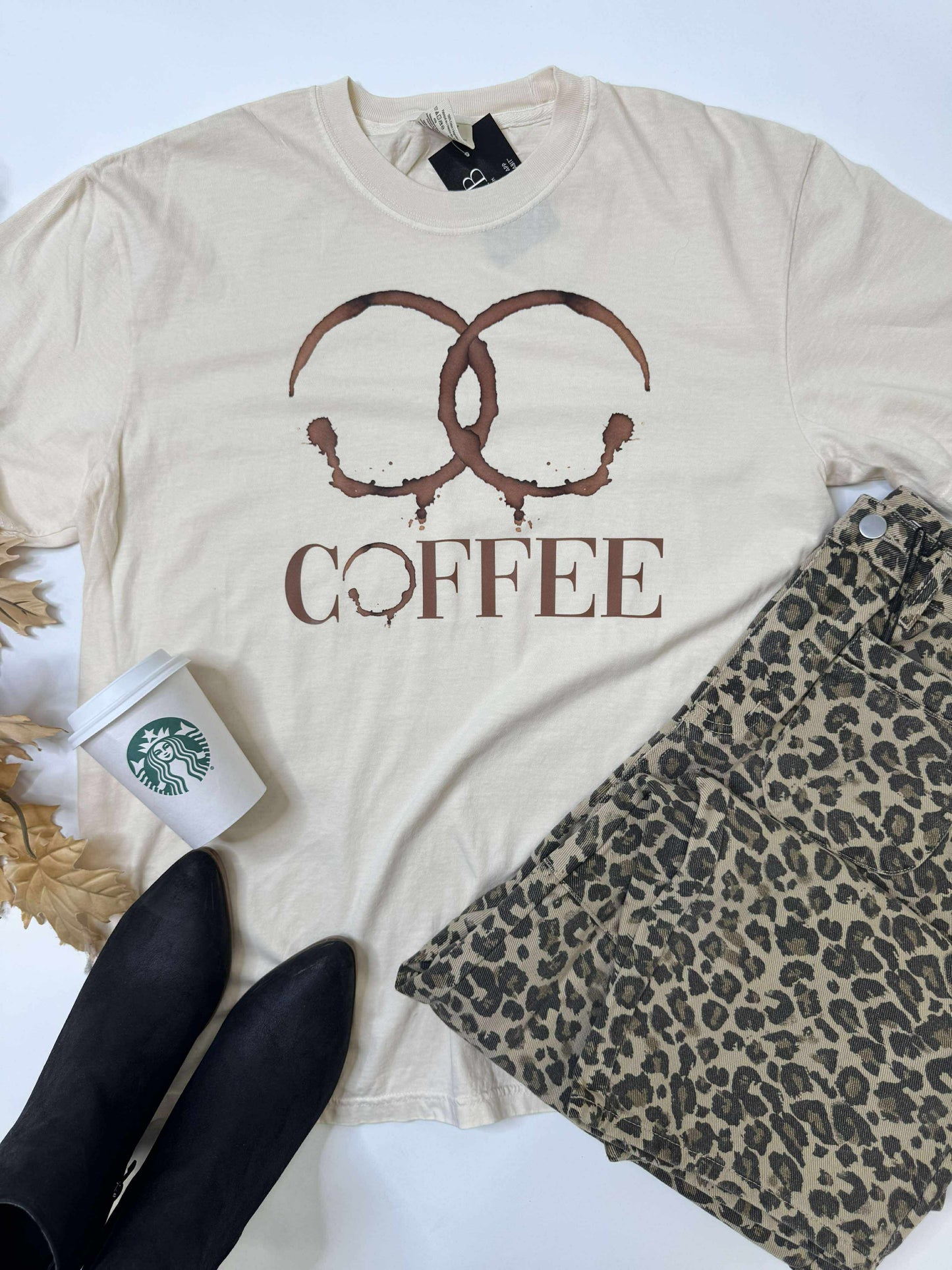 Beige t-shirt with 'COFFEE' design, Starbucks cup, and leopard print item on a light blue background