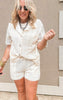 Two-piece ivory crochet outfit featuring a short-sleeve top with ruffled collar and coordinating shorts.