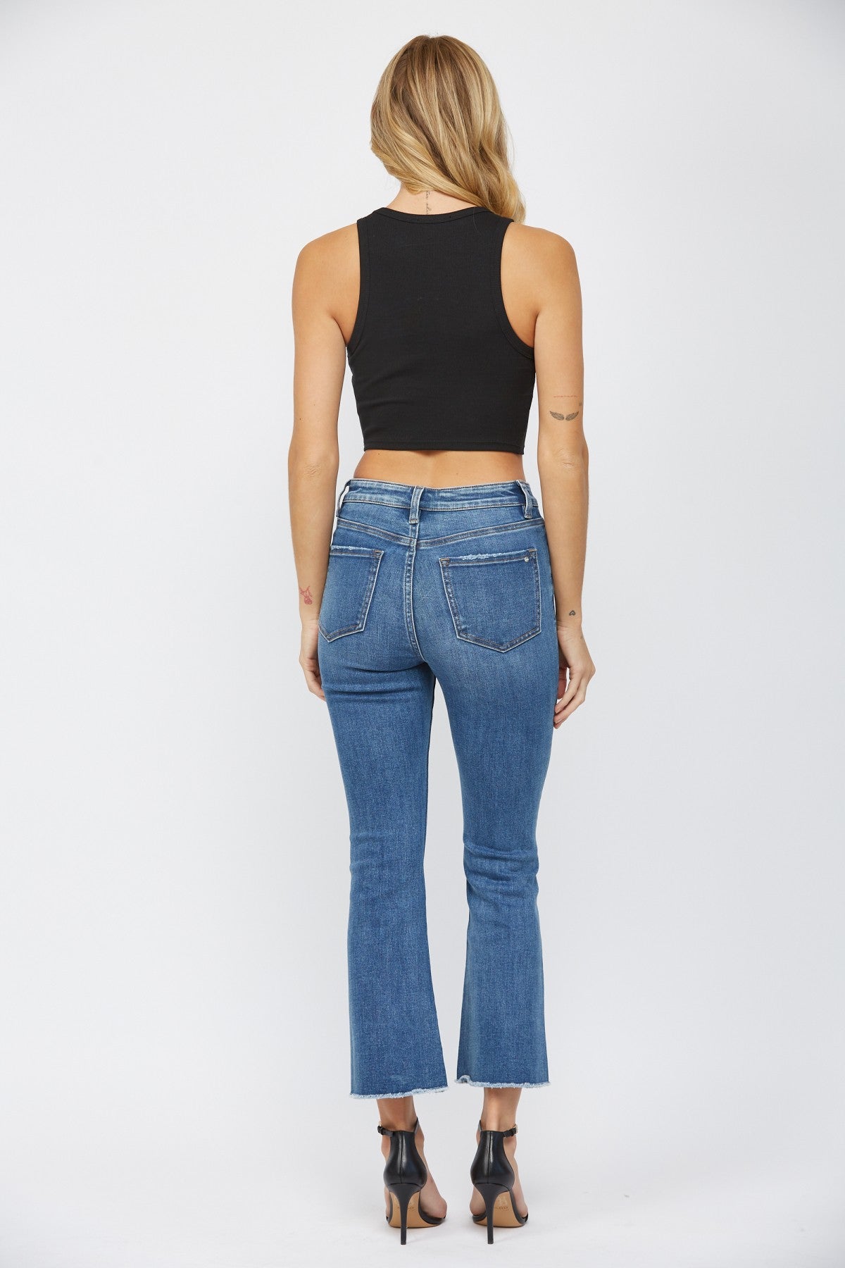 A woman standing backwards on white background showing the medium wash button fly mica denim jeans.